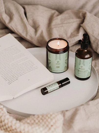 tray placed on bed with book, aromatherapy candle and two small bottles