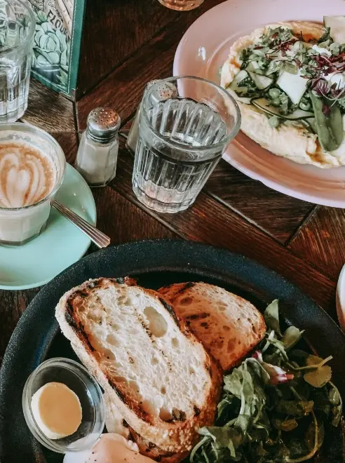 two plates of food, a coffee, glasses of water and a slat shaker on a table top