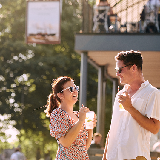 two people having a drink in the sun outside a pub in kew bridge called the steam packet
