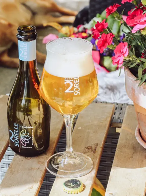 bottle and glass of beer on a table with cut flowers in a vase