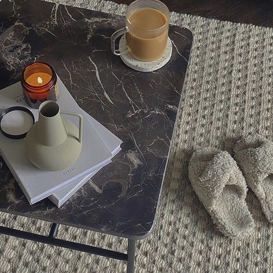 small table with a coffee, candle, books and slippers on floor next to it